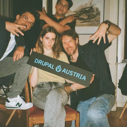 gruppe von 4 personen machen gang-signs in die kamera und halten ein schild hoch auf dem steht "drupal austria"