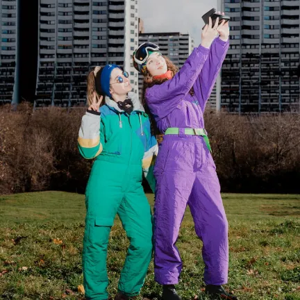 Lowfidelity Team Alexandra und Kristina in Vintage Kleidung auf einer grünen Wiese vor Alterlaa. Über den Personen steht Besinnliche, weiße Weihnacht.