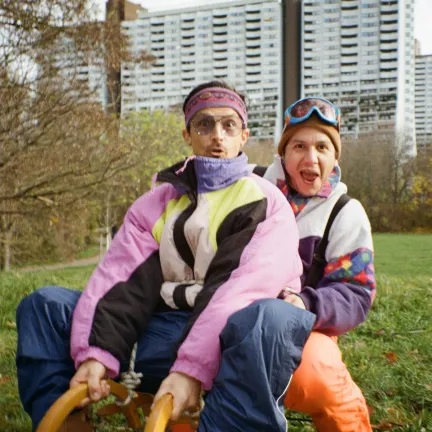 Daniel und Alex sitzen in Vintage-Winterbekleidung auf einem Schlitten in einer grünen Wiese
