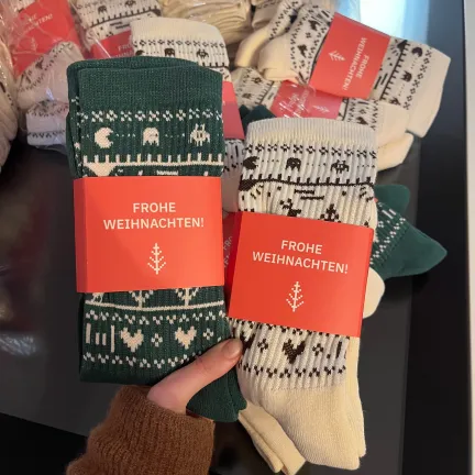 Eine Hand haltet zwei Paar Socken im lowfidelity Weihnachts-Design in die Kamera
