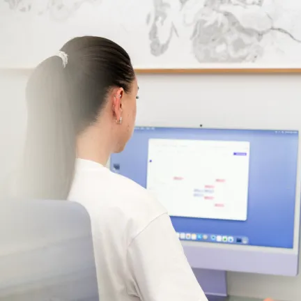Person sitzt mit dem Rücken zur Kamera an einem Computerarbeitsplatz.