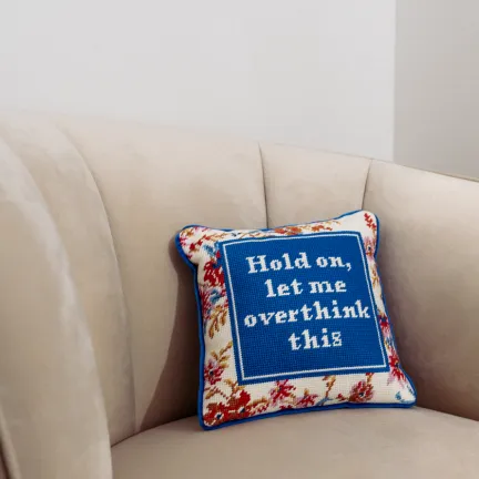 Besticktes Kissen mit der Aufschrift „Hold on, let me overthink this“ auf einem Sessel.